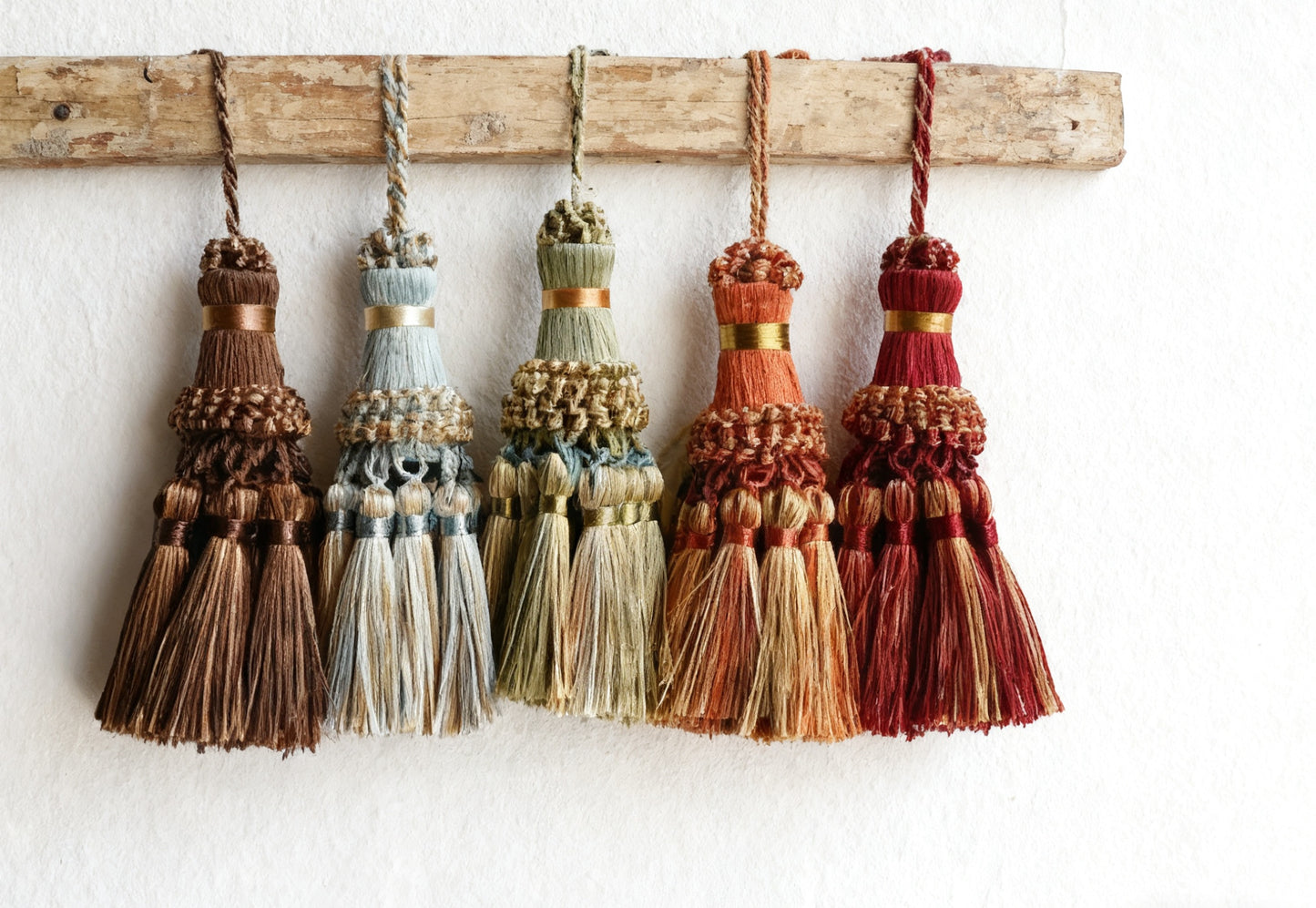 Set of colorful tassels hanging on a wooden rod against a white background